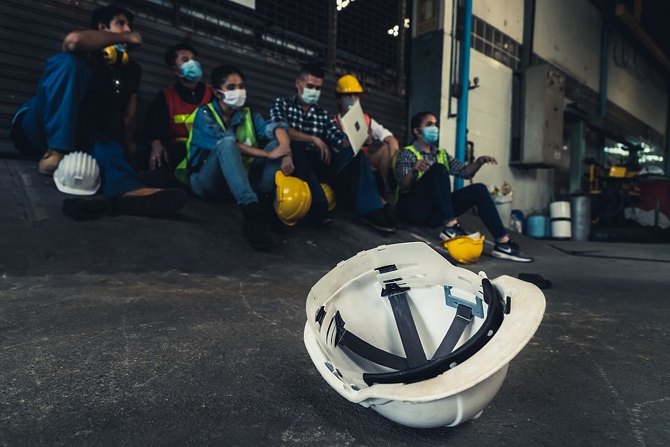 Bild von sitzenden Arbeitenden mit einem Helm im Vordergrund.