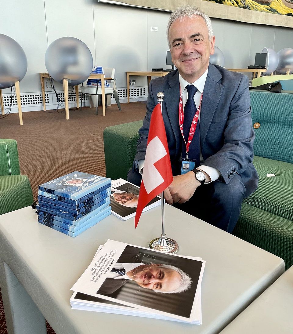 Professor Markus Schefer, an einem Tisch sitzend, auf dem eine kleine Schweizer Fahne steht.