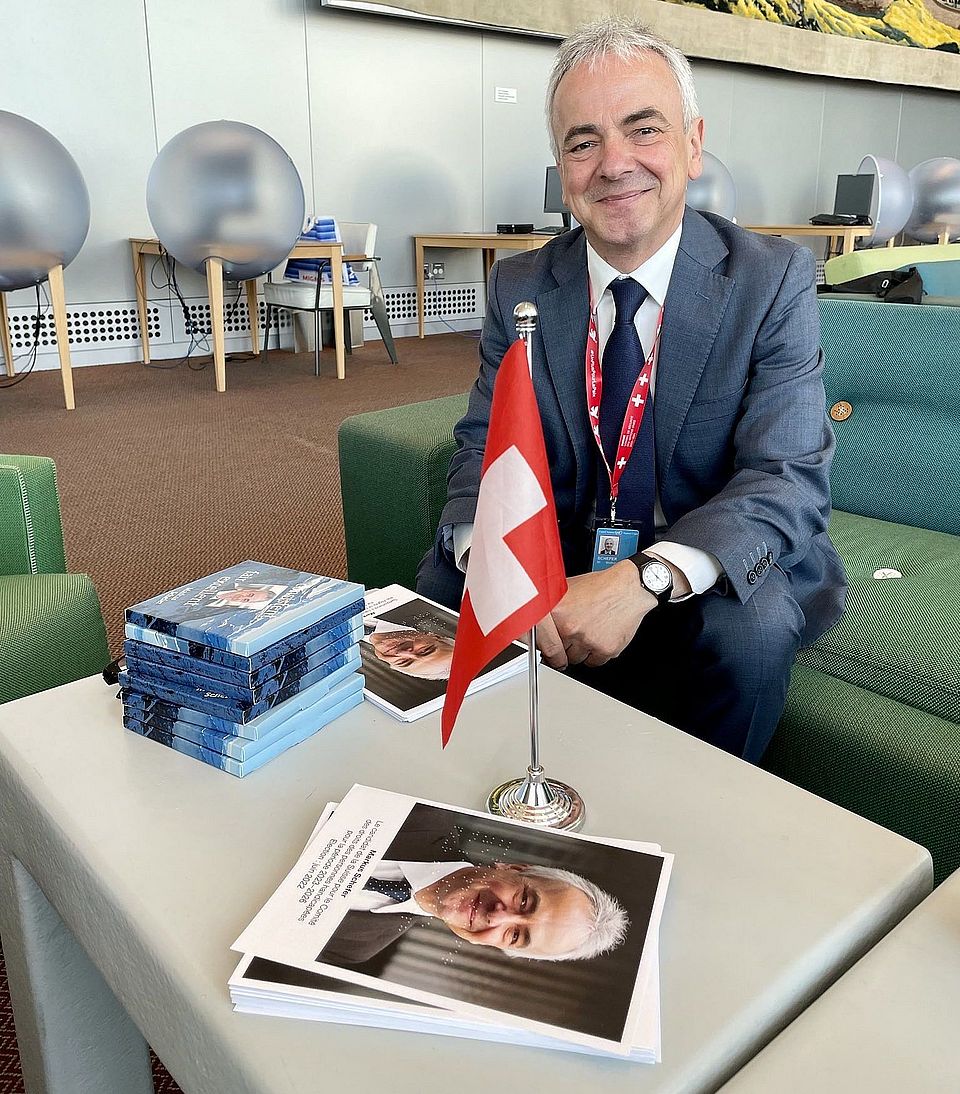 Professor Markus Schefer, an einem Tisch sitzend, auf dem eine kleine Schweizer Fahne steht.