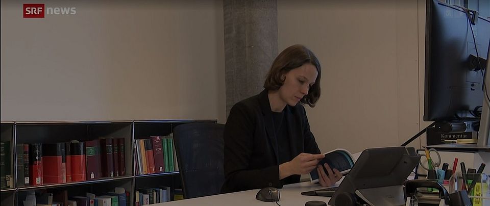 Cordula Lötscher, Lehrbeauftragte Privatrecht an den Universitäten Basel und St. Gallen, sitzt in ihrem Büro mit einem Buch in der Hand (SRF Newsbeitrag des Formats "10 vor 10" vom 09.12.2021).