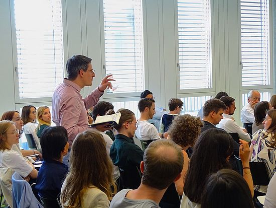 Szene der Veranstaltung Rousseau Lectures 2023 im Auditorium der Juristischen Fakultät, bei der ein Mithörer aus dem Publikum aufsteht, um eine Frage zu stellen.