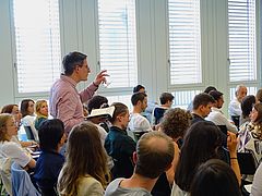 Szene der Veranstaltung Rousseau Lectures 2023 im Auditorium der Juristischen Fakultät, bei der ein Mithörer aus dem Publikum aufsteht, um eine Frage zu stellen.