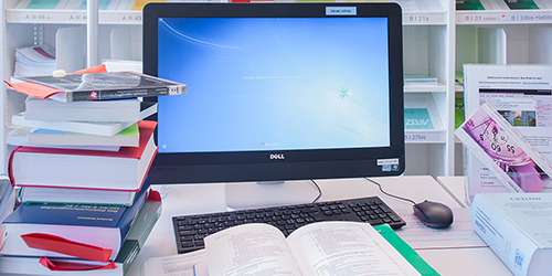 Bild mit Computer, vor dem ein aufgeschlagenes Buch liegt.