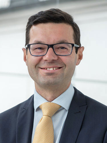 Porträt von Prof. Dr. Andreas Müller in dunklem Anzug mit gelber Krawatte.